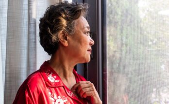 Older woman is shown staring out of a window