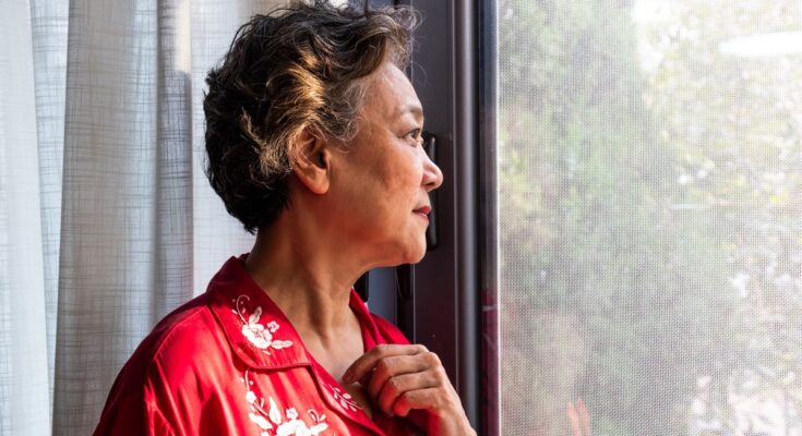 Older woman is shown staring out of a window